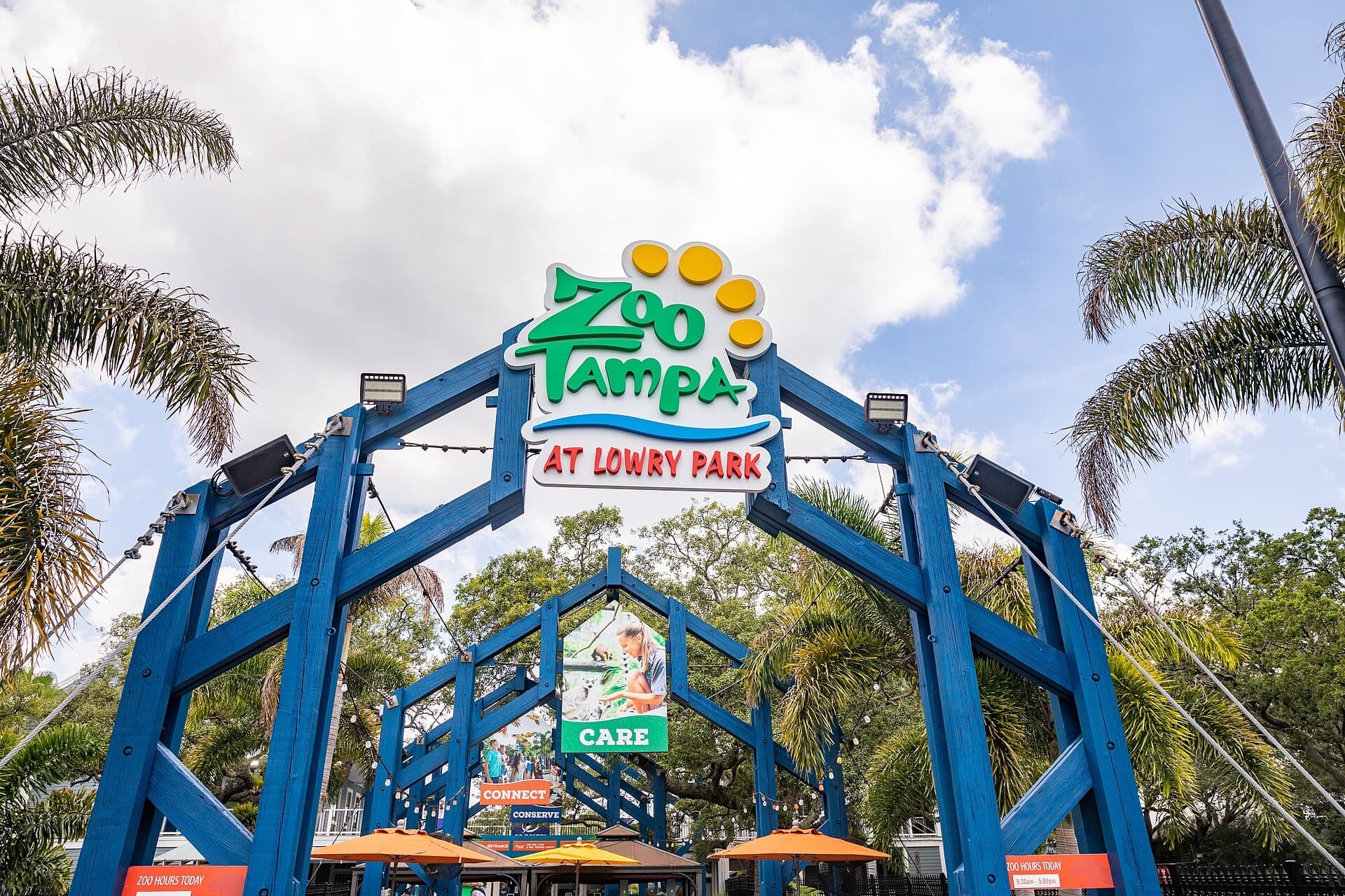The blue timber entrance arch at ZooTampa at Lowry Park with the zoo's logo sign and palm trees